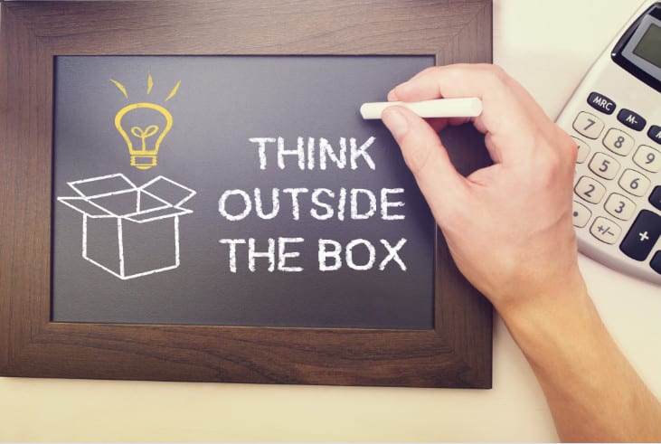 A person writing on a chalkboard that says " think outside the box ".