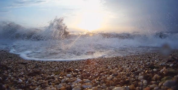 A beach with waves crashing on it and the sun shining.