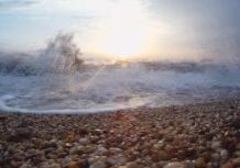 A beach with waves crashing on it and the sun shining.